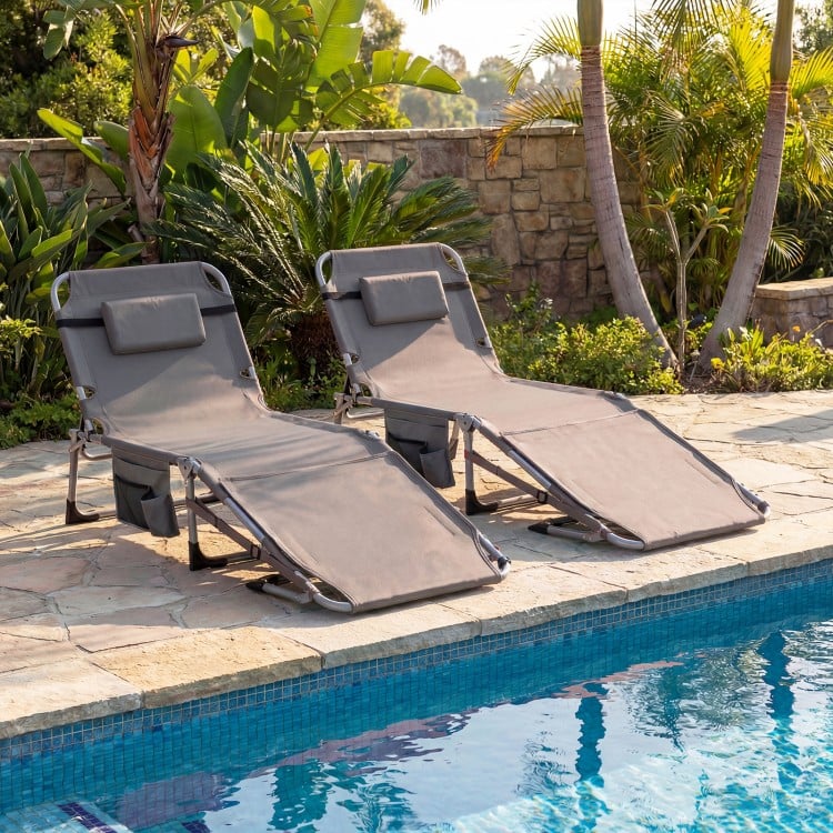 Two gray tanning chairs with face holes and arm openings by the pool, adjustable for sunbathing comfort.