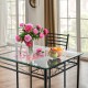 Dining table set in a bright room with flowers and fruit, showcasing the modern tempered glass top and metal frame.