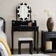 Black makeup dressing table with lighted mirror, cushioned stool, and four drawers for ample storage in elegant design.