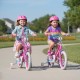 Two girls riding the pink 12-inch kids bike with adjustable handlebars and training wheels in a park setting.