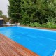 Rectangle swimming pool cover laid on wooden deck, 12-mil thick PE, designed to prevent debris and retain heat.