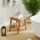 Teak wood shower bench with storage shelf, curved seat design, and adjustable foot pads for stability in the bathroom.