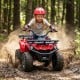 Child riding the red 24V Electric Ride On Quad through dirt, featuring LED headlights and wear-resistant wheels for.