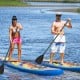 Two people paddle on inflatable stand-up paddle boards in a serene water setting, ideal for water sports and yoga.