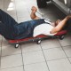 Low profile mechanic creeper with padded seat, red color, and 6 wheels, ideal for garage and auto repair tasks.