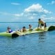 Floating water pad in green, 12’ x 6’, with four people enjoying relaxation on a lake under a sunny sky.