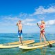 Two people paddle on inflatable stand-up paddle boards in clear water, ideal for summer water activities and stability.