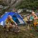 Camping scene featuring a blue 2-in-1 pop-up tent with two men enjoying outdoor relaxation and fire preparation.