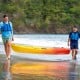 Two men carrying a yellow single sit-on-top kayak along the beach, ideal for fishing and leisure activities.