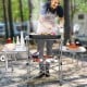 Foldable outdoor BBQ table with heat-resistant aluminum countertop and side shelves, perfect for camping and picnics.