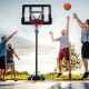 Basketball hoop system with adjustable height, shatterproof backboard, and two players shooting a basketball outdoors.