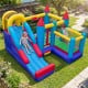 Inflatable bounce castle with slide, climbing wall, and basketball hoop for outdoor fun in the backyard.