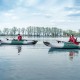 Two people kayaking on a sit-on-top fishing kayak in gray, featuring fishing rod holders and a comfortable padded seat.