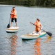 Two people paddling on 10' inflatable stand-up paddle boards in a lake, wearing life jackets for safety.
