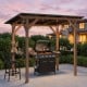 Cedar wood BBQ gazebo with a sloped metal roof and two side serving shelves, ideal for outdoor gatherings and parties.