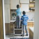 Two children using a 2.75 feet folding step stool with anti-slip pedals for reaching high kitchen cabinets.