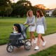 Two women walk a gray 3-wheel pet stroller with a dog, showcasing its foldable design and mesh ventilation.