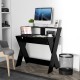 Small black computer desk with raised monitor stand, storage drawer, and X-shaped legs for stability in a modern.