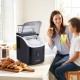 Countertop ice maker in black with external tank, making ice cubes while a woman and child enjoy drinks at a kitchen.
