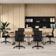 Ergonomic black desk chair with lumbar support and armrests, shown in a modern office setting around a wooden table.