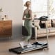 Folding treadmill with LCD display and 12 preset programs, showcasing a user walking in a modern living room setting.