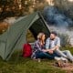 Foldable 2-person camping cot tent in green, set up by a lake, ideal for camping and outdoor adventures.