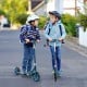 Two kids riding folding aluminum alloy scooters with adjustable heights on a residential street, showcasing safety.