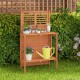 Folding garden potting bench with teak oil finish, featuring 2-tier storage shelves for plants and tools in a backyard.
