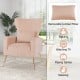 Velvet upholstered wingback chair in pink with lumbar pillow and golden metal legs, perfect for reading and relaxing.