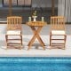 Two outdoor folding chairs with beige seat cushions and a round acacia wood table, perfect for poolside dining.