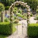 Heavy-duty black metal garden arch with gate, adorned with pink roses, perfect for supporting climbing plants and.