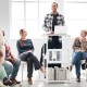 Height adjustable mobile computer stand-up desk in use during a presentation, featuring a white finish and bottom.