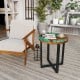 Round teak wood end table with epoxy resin top, featuring X-shaped legs, ideal for outdoor use on patio or balcony.