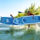 Two people carrying an inflatable stand-up paddle board with a stylish coco motif, ideal for all-skill levels on water.