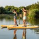 Two people paddle on inflatable stand-up paddle boards in a serene water setting, showcasing stability and versatility.