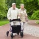 Height adjustable purple rollator walker with seat, featuring all-terrain wheels, used by seniors in a park.