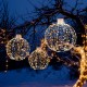Three decorative Christmas LED light balls in golden hues, featuring warm and white lights, suspended in a snowy.