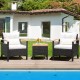 Two single chairs with off-white cushions and a small acacia wood table in a patio setting by the pool.