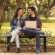 Two people sitting on a 47-inch outdoor bench with a slatted seat, made of weather-resistant HDPE, in a garden setting.