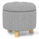 Round gray upholstered ottoman with solid rubber feet, featuring cushioned seat and storage space for versatile use.