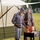 Two men grilling under a beige 10 x 10 feet screened canopy tent, ideal for camping and outdoor activities.