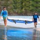 Two men carrying a blue inflatable kayak set with oars along the beach, perfect for outdoor water adventures.