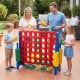 Jumbo 4 in a Row game set with family playing outdoors, featuring red and green chess pieces for fun group activity.