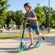 Boy riding a blue foldable kick scooter with large light-up wheels, designed for kids and teens, in a park setting.