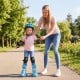 Child wearing blue adjustable roller skates with light-up wheels, assisted by an adult in a park setting.
