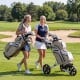 Two women walking on a golf course with a khaki molded lock top golf cart bag featuring 14-way dividers and multiple.