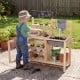 Child playing at the Mud Kitchen Playset, exploring gardening with 12 plant cups and a spacious sink for outdoor fun.