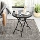 Round black folding side table with tempered glass top, perfect for indoor and outdoor use, shown in a living room.