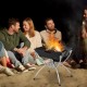 3-in-1 camping campfire grill with stainless steel construction, set up for BBQ, surrounded by friends by the fire.