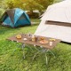 Folding camping table with wood-grain tabletop set up outdoors, ideal for hiking, picnics, and BBQs.